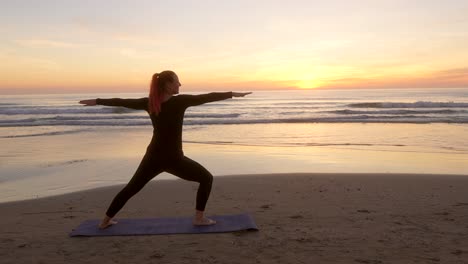 Mujer-En-La-Estera-Realizando-Dos-Poses-De-Guerrero-En-La-Playa-Durante-El-Amanecer