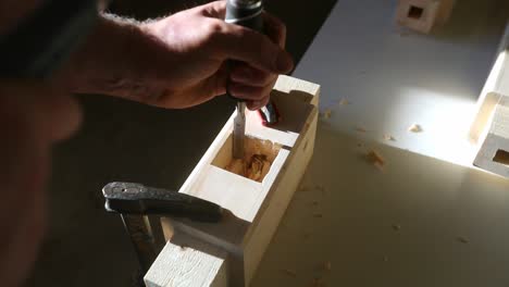 A craftsman uses a hand chisel and hammer to mortise a piece of furniture in slow motion