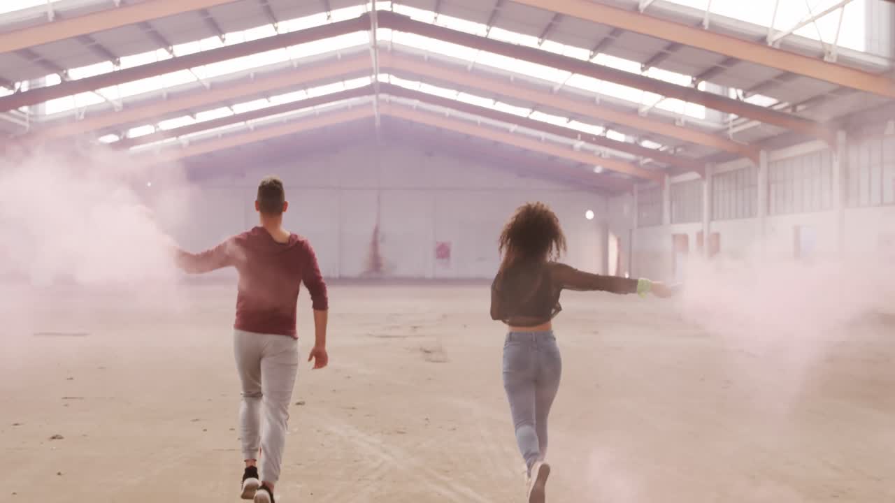 Dancers in an empty warehouse holding smoke grenade