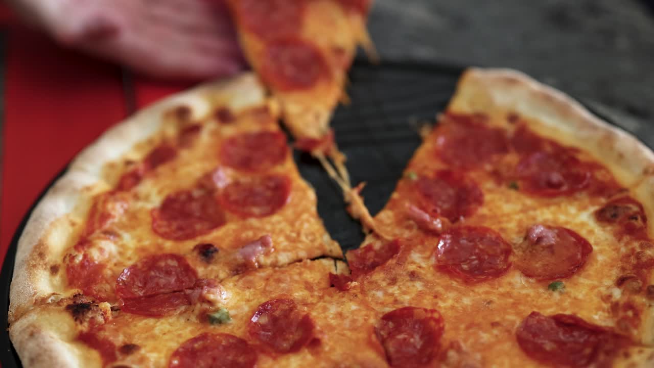 손은 페페로니 피자의 조각을 들고, 적적한 치즈와 활기찬 빨간 바탕을 보여줍니다.