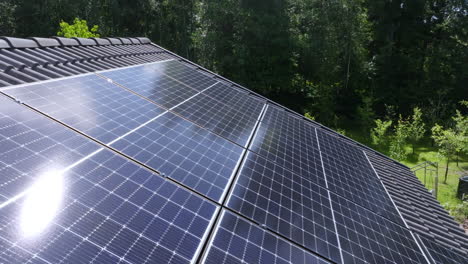 Aerial view low over reflecting solar panels on a house roof, sunny, summer day