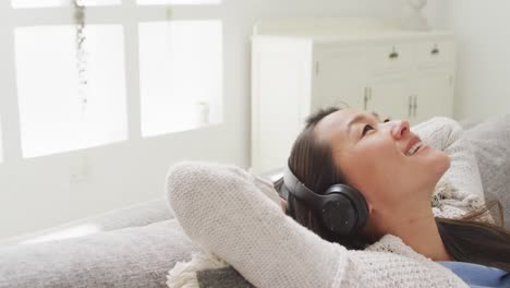 mujer asiática feliz acostada en el sofá, descansando con auriculares en casa