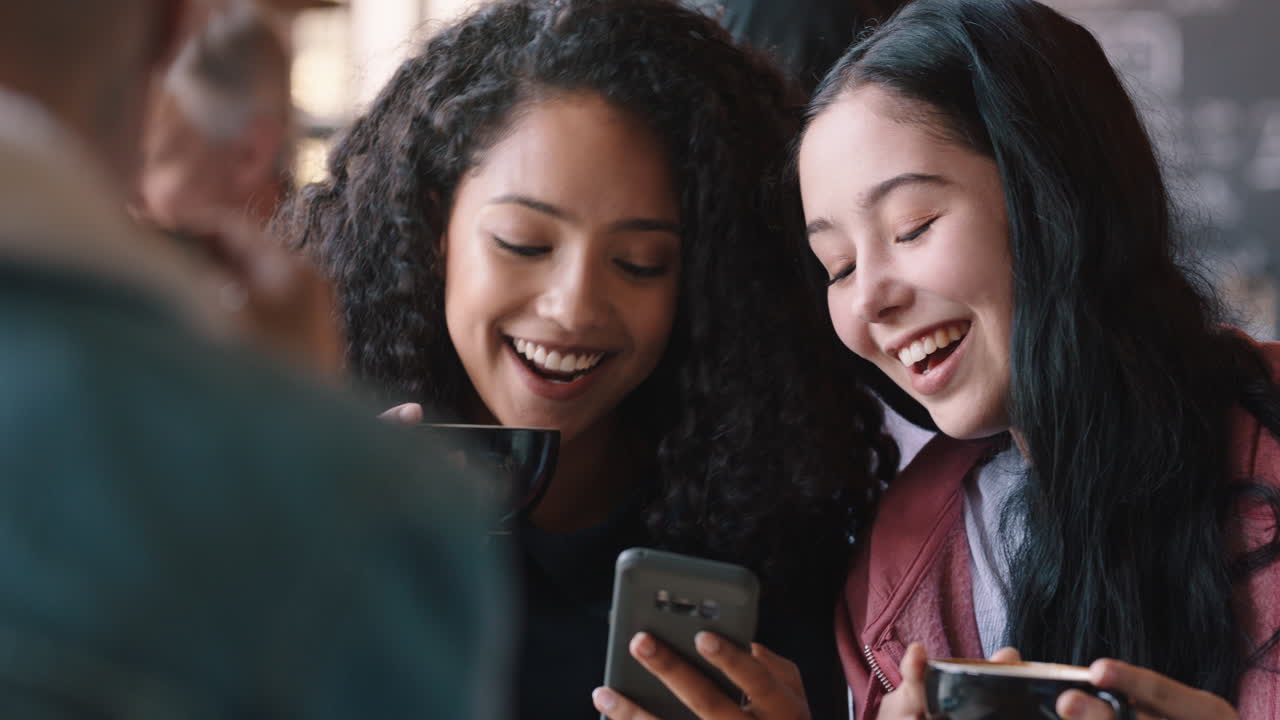 happy teenage girl friends using smartphones drinking coffee in cafe texting hanging out sharing gossip enjoying chatting together
