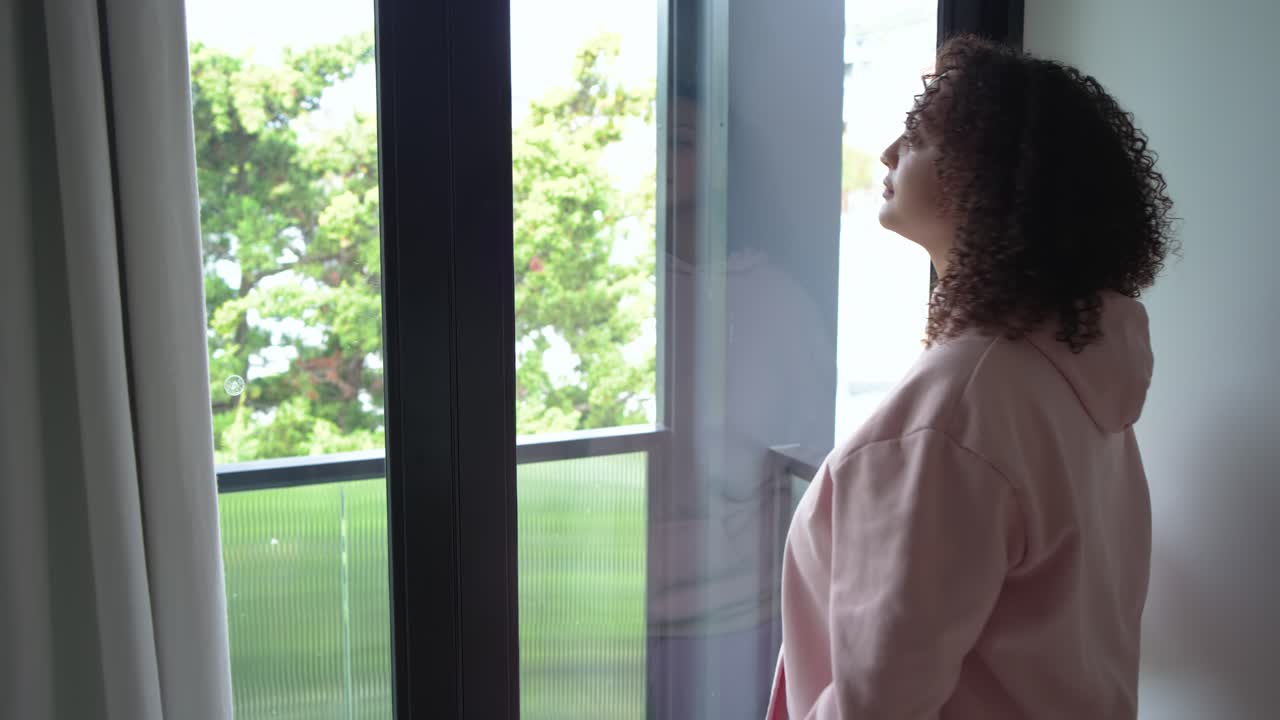 Una donna in rosa sta tirando la tenda alla porta, uscendo sul balcone in cerca di calma inspirando.