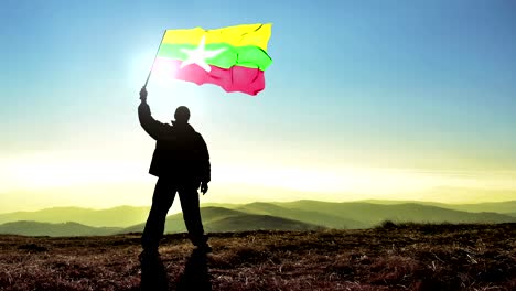 exitoso hombre silueta ganador agitando bandera de birmania en la parte superior del pico de la montaña. fondo de bucle cinemagraph