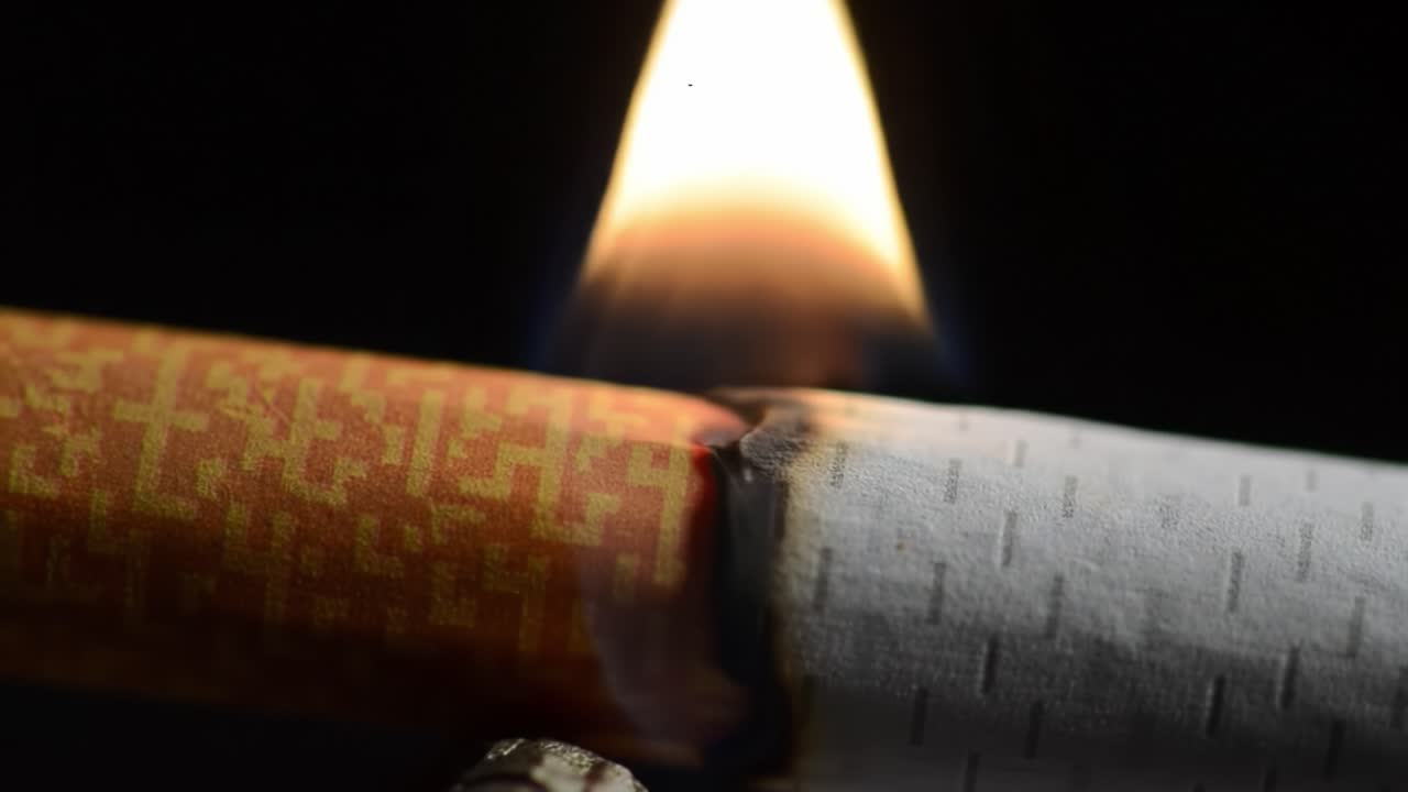 Close-Up of a Cigarette Burning with Flames Erupting from the Lit End, Capturing the Process of Combustion and Smoke Generation in Detail