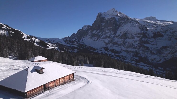 pushing in over alpine snow fields over alpine barns with picturesque view of wintery Mount Wetterhorn in Grindelwald, Switzerland