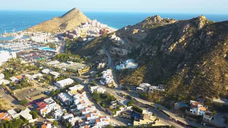 Drone-shot-of-resorts-on-Playa-El-Médano-with-mountains-in-the-distance-in-Cabo-San-Lucas-Mexico,-wide-and-rotating