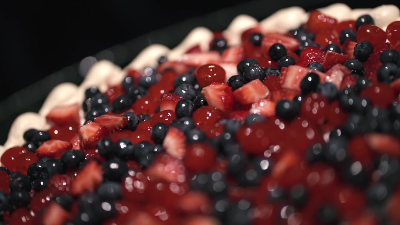 Postre de tarta de frutos rojos con fresas (Fragaria × ananassa) y arándanos (Vaccinium corymbosum) cubierto con un glaseado brillante, con poca profundidad de campo y un bokeh pronunciado, toma macro extrema, revelación con paneo.
