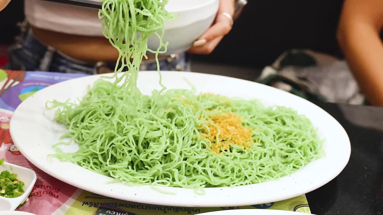 Person serving green noodles with chopsticks