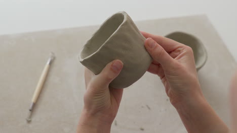 skillfully engraving a clay cup's bottom with a hands, creating intricate texture in a charming studio