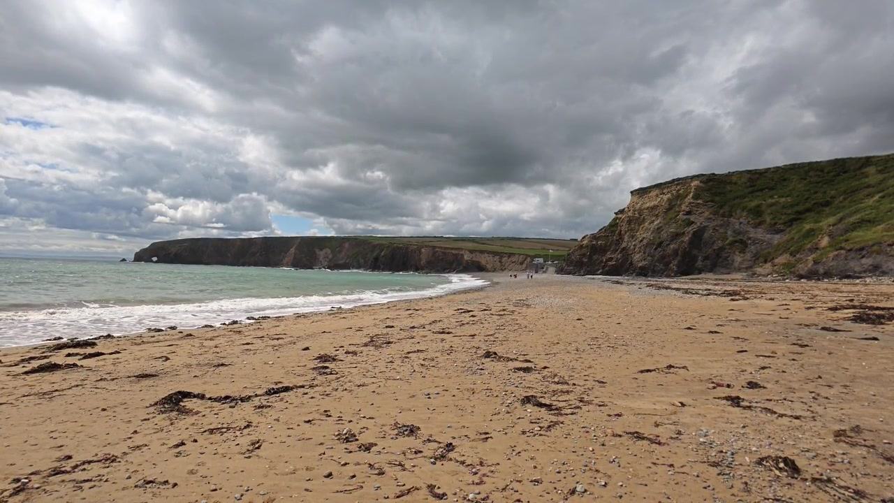 Irlanda, luoghi epici: lunga spiaggia con persone che camminano, nuvole di pioggia in avvicinamento prima della pioggia.