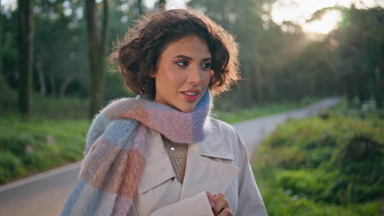 bruneta contemplativa de pie en la naturaleza al atardecer con una expresión serena de primer plano.