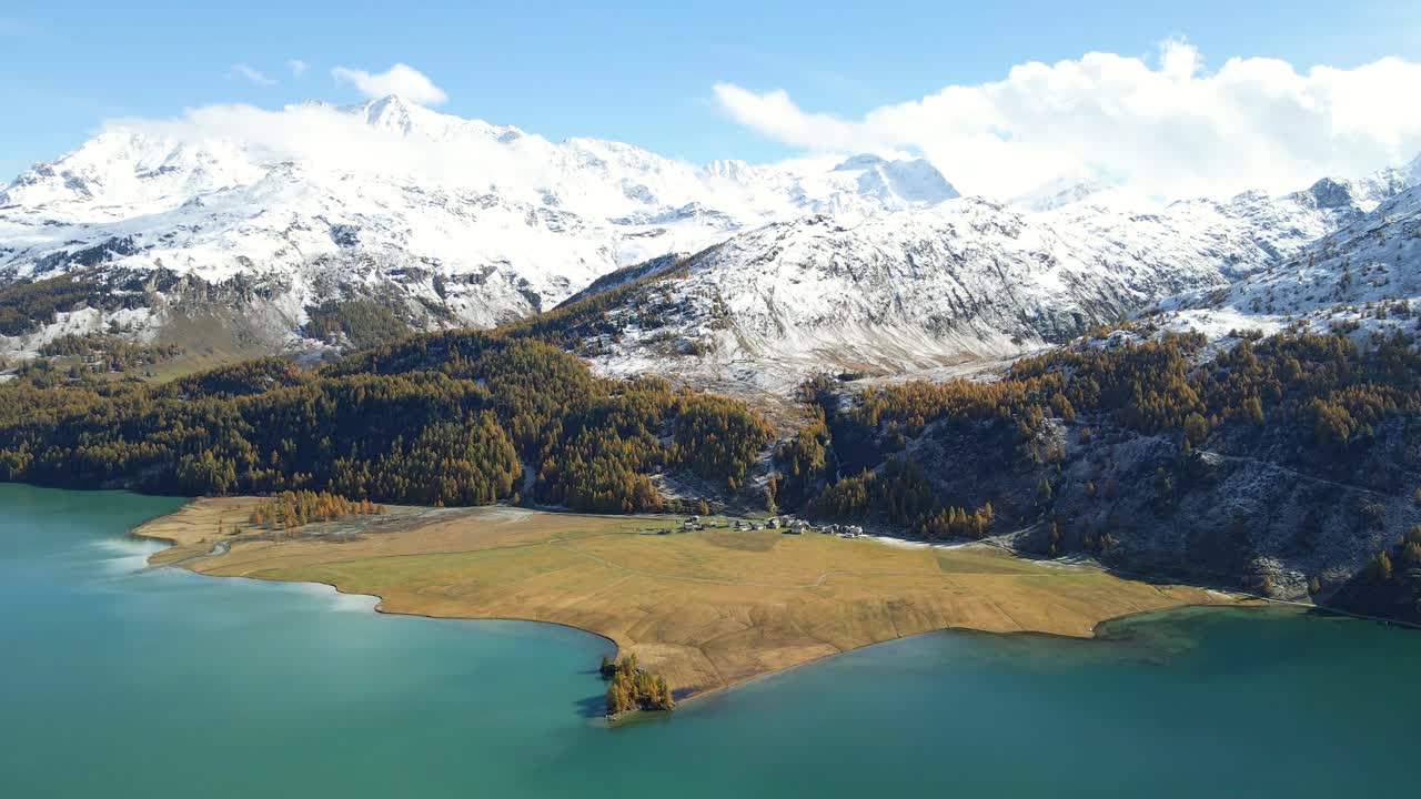 Aerial view of the Lake Sils (Silsersee) with the mgestic bakcdrop of the snowy mountains and clouds, Isola in Upper Engadine, Grisons, Switzerland.Autumn