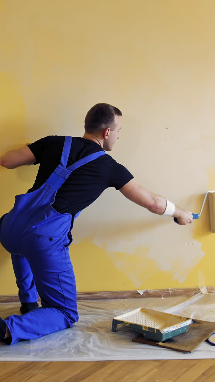Young worker painting wall in room. Repair, building and home concept. Vertical video