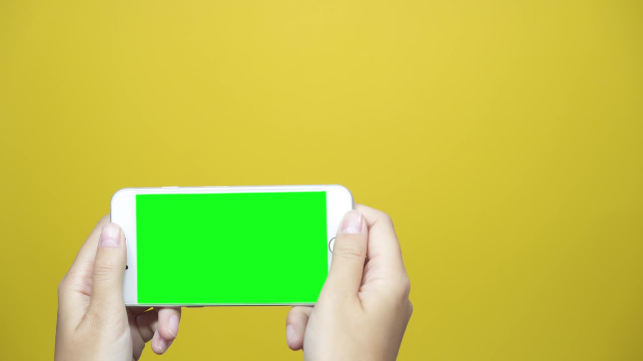노란색 테이블 배경에 녹색 화면을 가진 스마트 폰을 사용하는 여성. 여성 손이 페이지를 스크롤하고, 터치 스크린을 합니다.