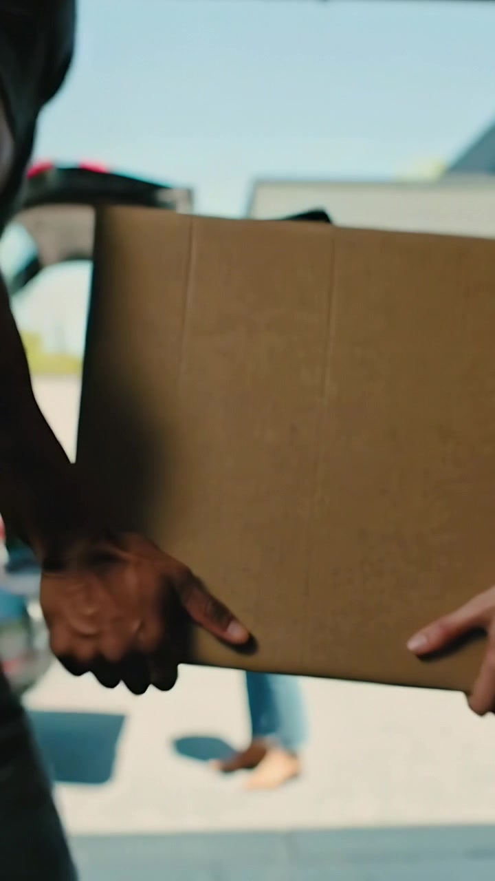 Vertical video: Carrying two adults walking box with open trunk to house door, unloading clothes
