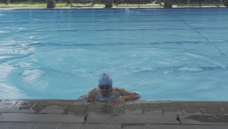 young man swimming frog style, reaching border of pool and climbing out from poolside