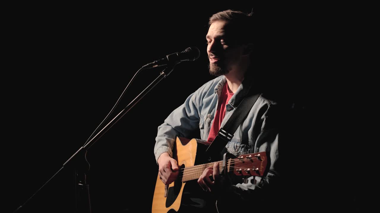 un músico está tocando la guitarra en un gran escenario con miembros de la audiencia sosteniendo linternas en el fondo. el auditorio está lleno de hermosas luces parpadeantes.