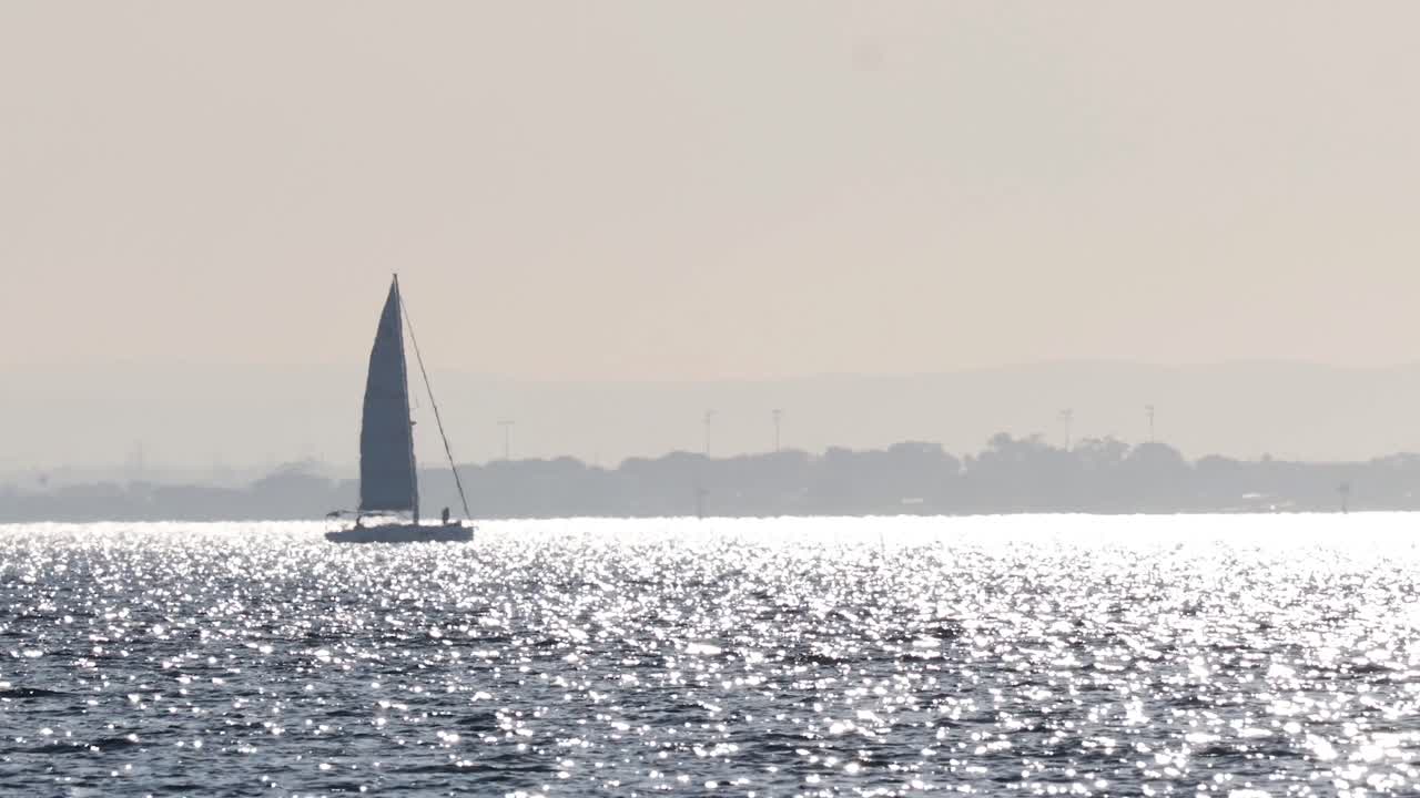 A sailboat moves across the shimmering ocean
