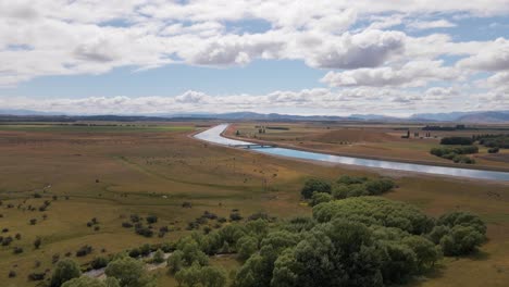 Vuelo-De-Drones-Acercándose-A-Un-Puente-Sobre-Un-Canal-Hidroeléctrico-Hecho-Por-El-Hombre-En-La-Distancia-Dentro-De-Un-Paisaje-Vasto-Y-Seco