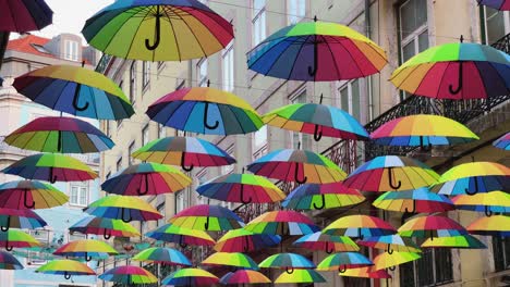 rainbow colored umbrellas dangle over pink street in lisbon portugal