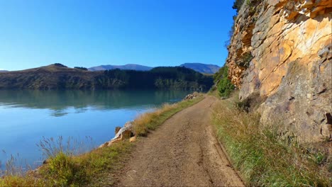 Walking-on-coastal-track-in-harbor-beside-interesting-wall-of-volcanic-rock-on-a-beautiful-day---Governors-Bay-Track,-Banks-Peninsula