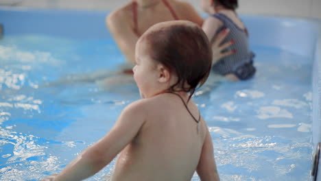 Happy-middle-aged-mother-swimming-with-cute-adorable-baby-in-swimming-pool.-Smiling-mom-and-little-child,-newborn-girl-having-fun-together.-Active-family-spending-leisure-and-time-in-spa-hotel.