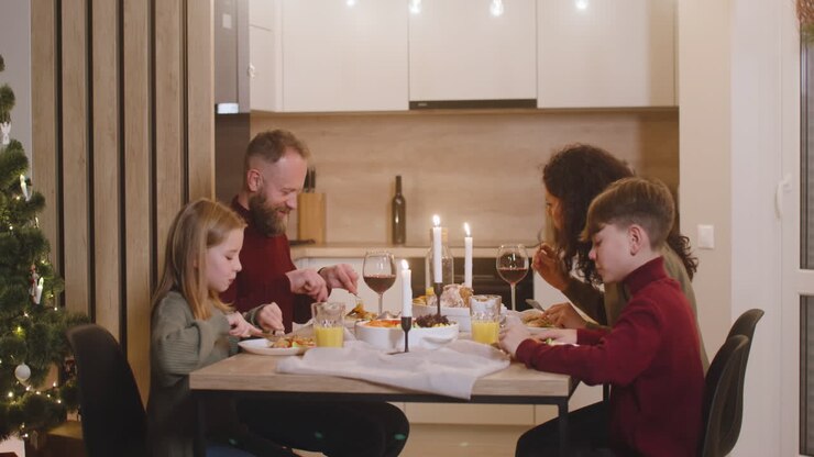 Famiglia di genitori e due figli che cenano a Natale seduti al tavolo della cucina.