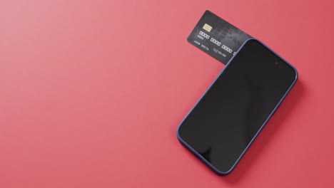 Video-of-smartphone-with-blank-screen,-boxes-and-credit-card-with-copy-space-on-red-background