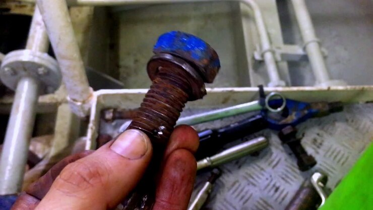 Male hand covered in oil and grease holding a rusty bolt