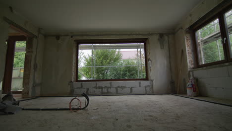 amplia toma en un sitio de construcción, la sala de estar se renueva, las pistas de la cámara hacia una ventana enorme, hermoso jardín con arbustos visibles