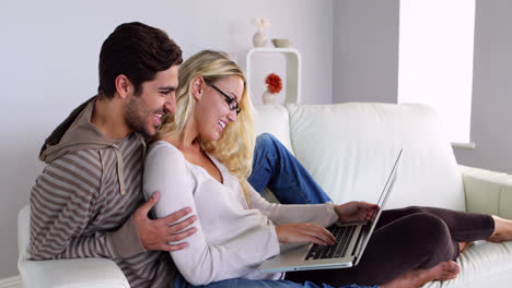 pareja feliz sentada en el sofá usando la computadora portátil
