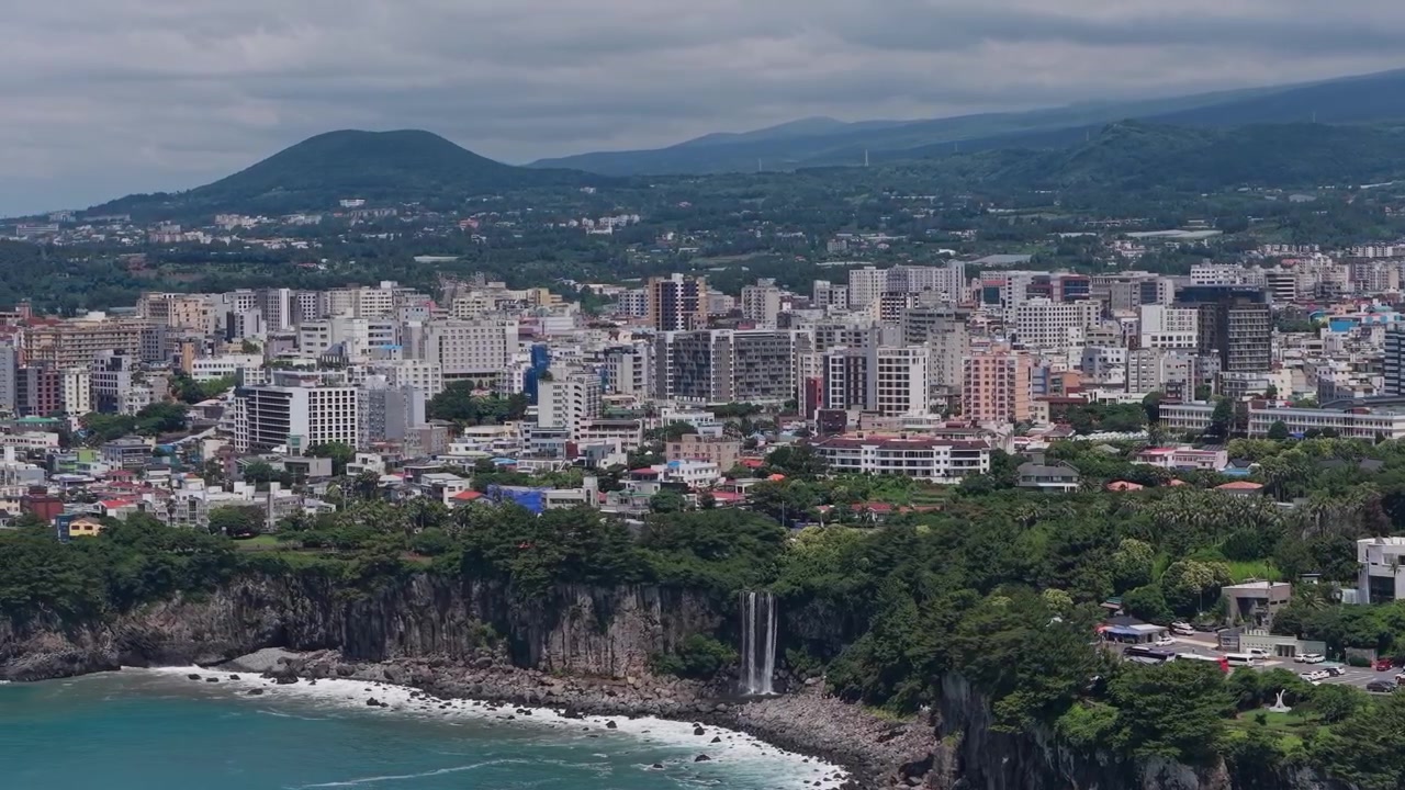 Carrellata orizzontale lenta verso sinistra su Seogwipo, Isola di Jeju, Corea del Sud, che mostra scogliere costiere ed edifici cittadini