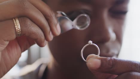 African-american-female-worker-inspecting-ring-with-magnifying-glass-in-workshop-in-slow-motion