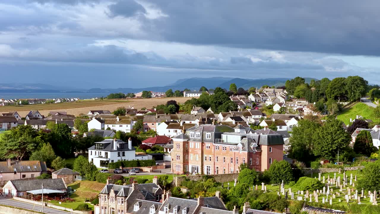 Wide shot slowly pans over Rosemarkie village, beachfront houses, and dramatic Highland landscape under sunlight