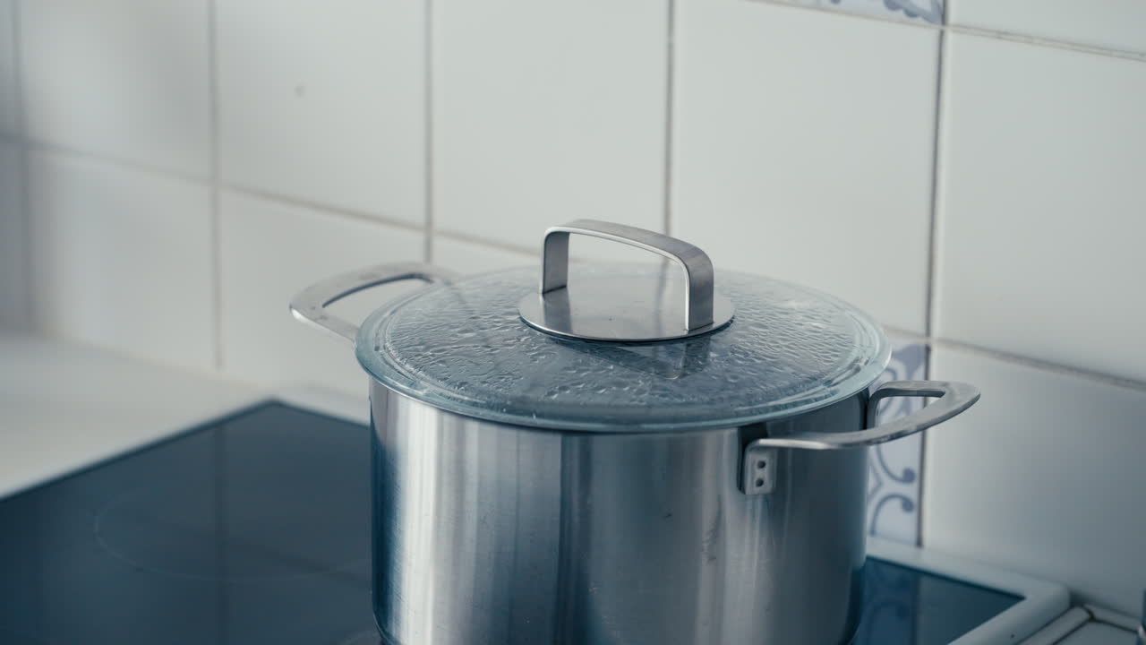 Water Boils In Large Iron Pot covered with transparent Lid on The Stove in white Kitchen in slow motion