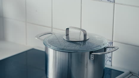 water boils in large iron pot covered with transparent lid on the stove in white kitchen in slow motion