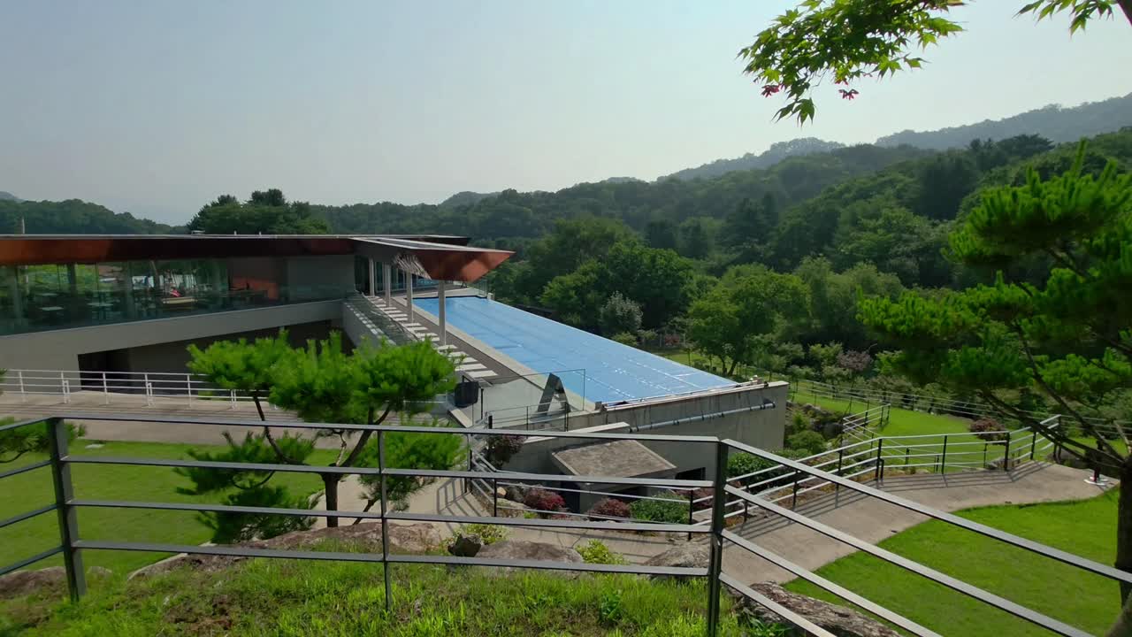 A cinematic push-in shot reveals the modern welcome center of Glam Tree Resort in Gapyeong, surrounded by lush forest and mountain views, highlighting the unique architecture and natural setting