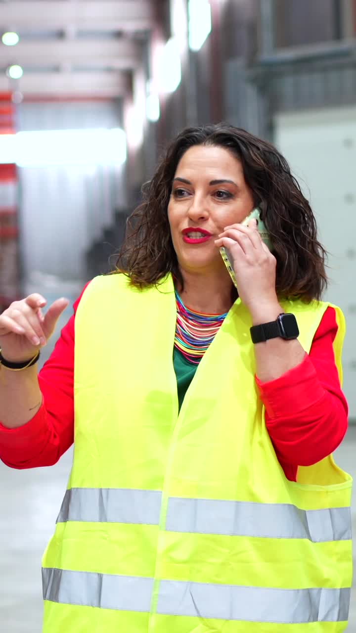 Woman in a safety vest talking on the phone in a warehouse