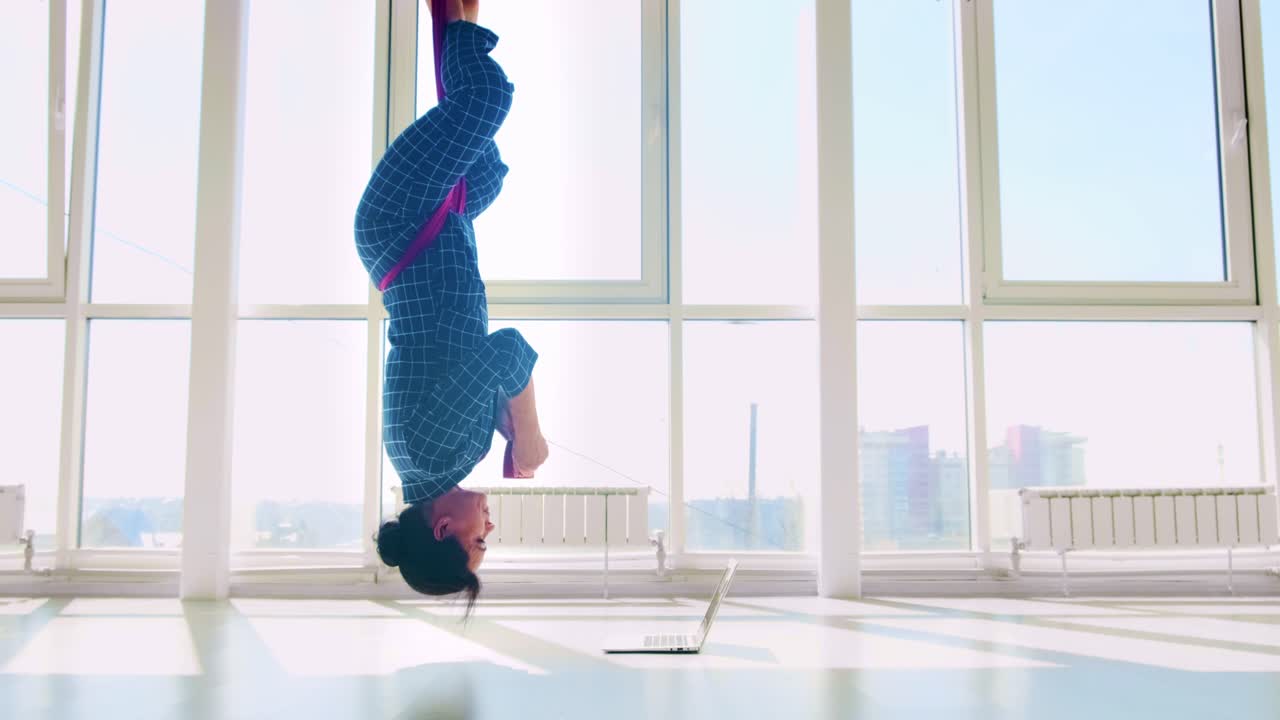 Aerial Yoga Practice: A Focused Individual Engaging in Upside-Down Pose in a Bright Room, Balancing Mind and Body Through Innovative Techniques