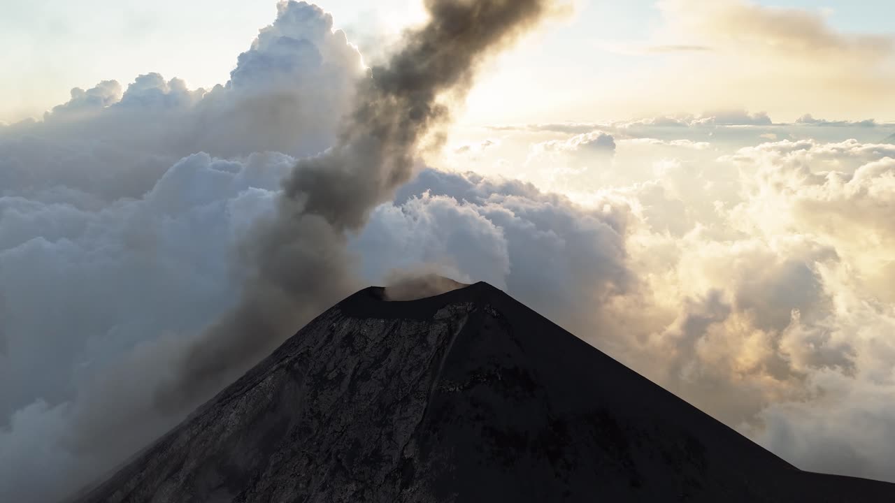 Volcano peak above a white cloudscape with dark smoke, aerial view