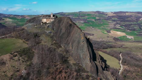 aerial footage of pietra perduca, volcanic rock, church set at top stone immersed in countryside landscape, cultivated land in val trebbia bobbio, emilia romagna, italy