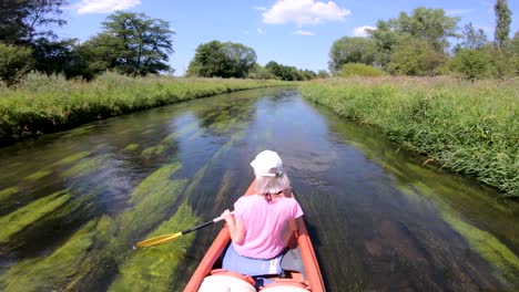 a girl in a canoe drifting on a european creek with colorful aquatic plants underwater and beautiful nature around