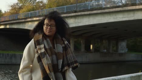 curly black woman waiting outside in the autumn cold in front of a bridge