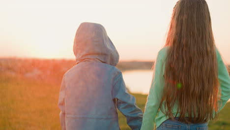 kids boy and girl hold hands in rain at riverside little brother and elder sister look at river at