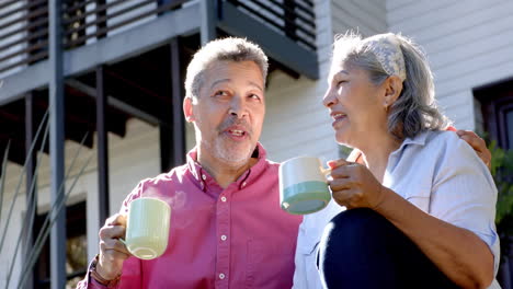 happy biracial senior couple sitting and drinking tea in sunny garden