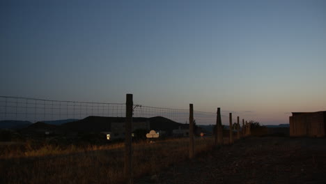 Coche-En-La-Carretera-Rural-Con-Valla-De-Alambre-Metálico-Junto-A-La-Vista-Del-Atardecer