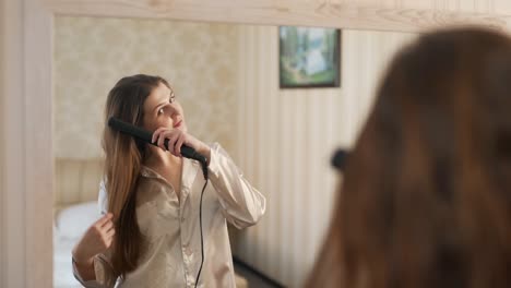 young woman in the mirror straightens with a curling iron