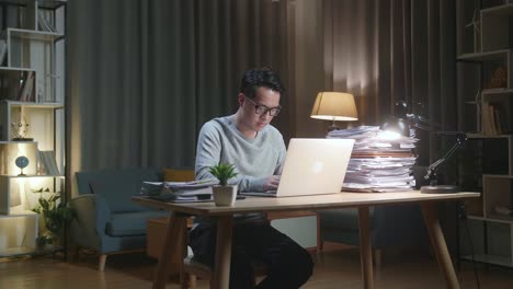 asian man typing laptop computer while working with documents at home